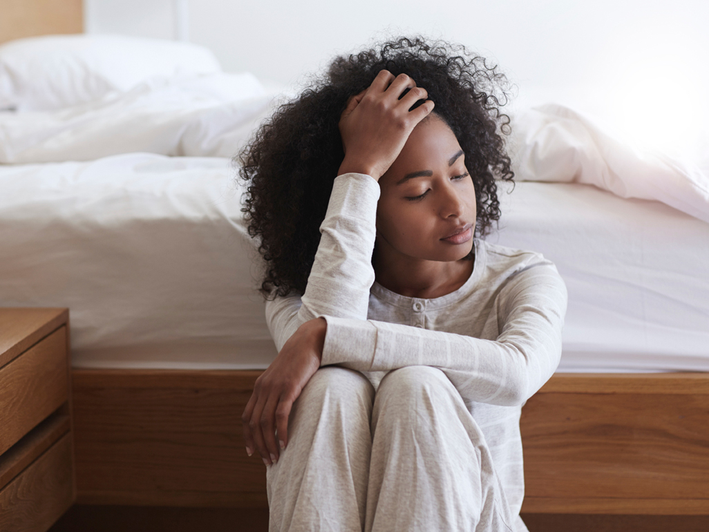 woman sitting on the floor next to her bed with feeling ill