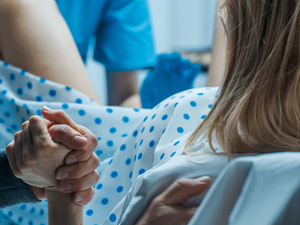 A pregnant woman in a hospital bed, in labor, squeezing a partner's hand.