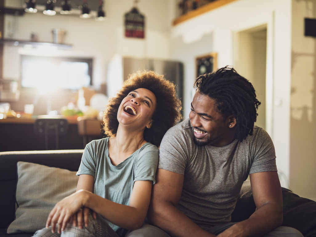 man and woman sitting together on couch laughing