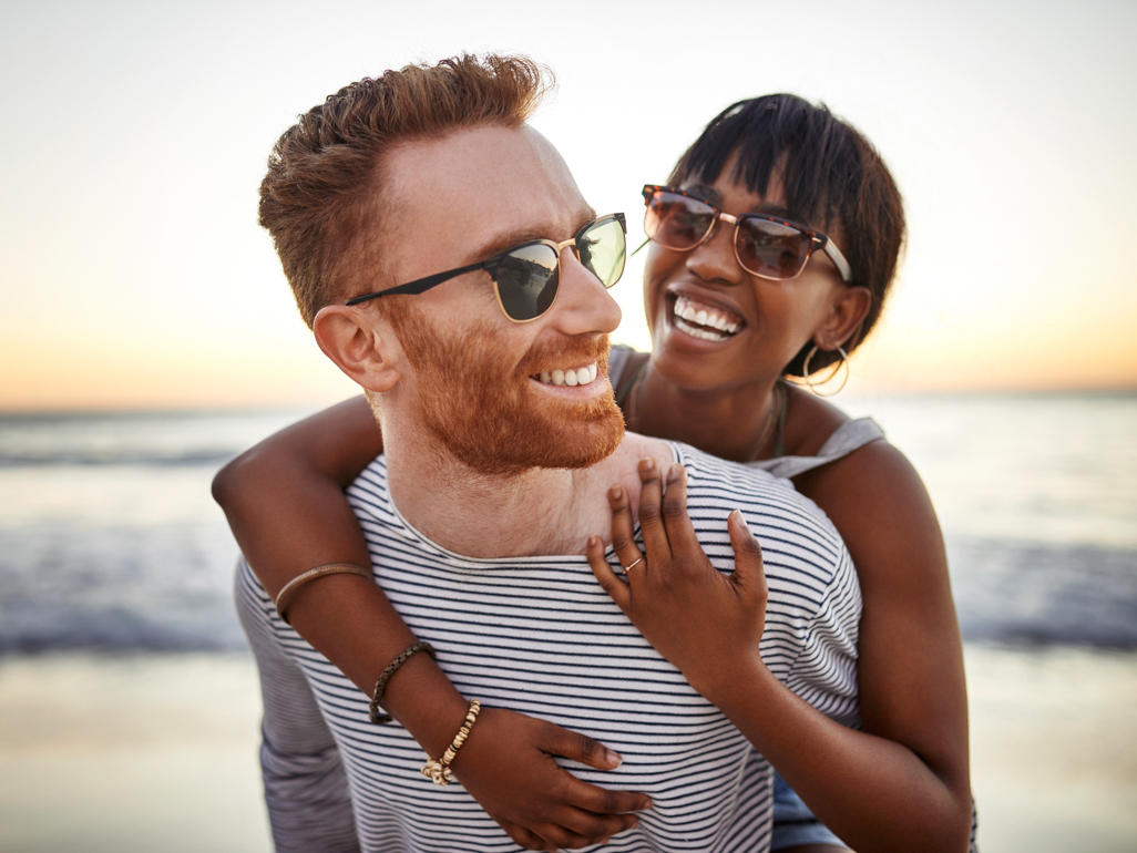 woman hugging man from behind while standing by the ocean