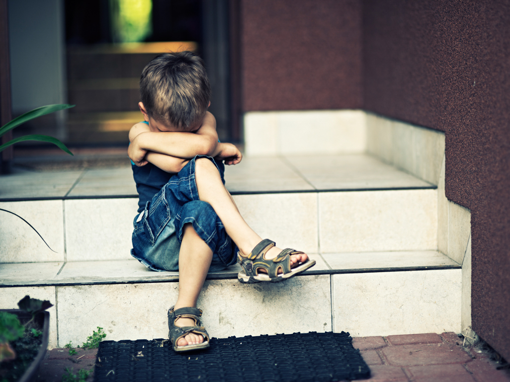 little boy sitting on steps with head buried in his arms