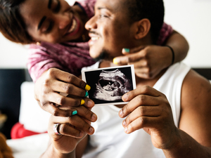 man holding an ultrasound baby photo, while a woman is hugging him from behind