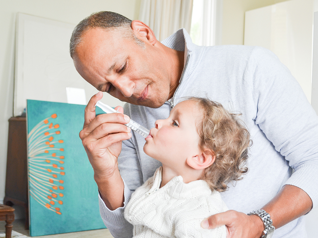 dad giving little boy medicine in his mouth